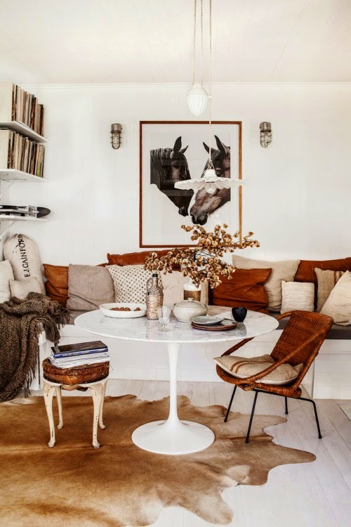 metalowy fotel z bambusową plecionką,okragły biały stół na jednej nodze,stylowy taboret,sofa z biało-rudymi poduszkami,nowoczesna fotografia,eklektyczny salon z kominkiem,stylowy mix w salonie,biało-brązowa aranżacja salonu w eklektycznym stylu