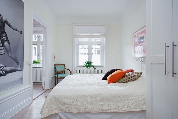 ozdobne poduszki na łóżku w sypialni,pomarańczowa poduszka,stylowe turkusowe krzesło,aranżacja skandynawskiej sypialni,ceramiczny piec w sypialni,okrągły piec skandynawski,duże fotografie na ścianach