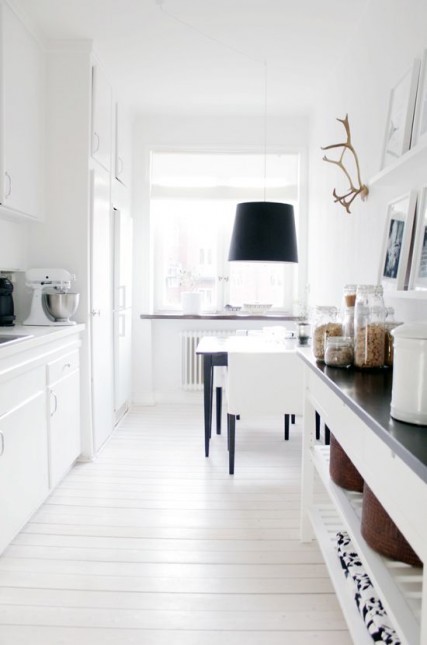 aranżacja białej kuchni,skandynawska kuchnia,wąska kuchnia,czarna lampa nad stołem w kuchni,biała podłoga w kuchni