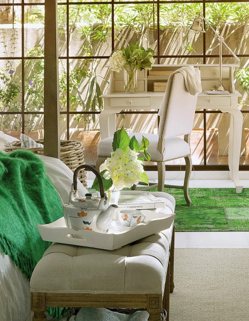 zielone dodatki w sypialni,pikowana ławka we francuskim stylu,białe tace,porcelanowy serwis do kawy i herbaty,śniadanie w sypialni,beżowy dywan tkany,zielony dywan patchwork w stylu vintage,turkusowy pled z frędzlami,francuskie krzesło w beżowej tapicerce,biały sekretarzyk biurko,stylowe biurko biale,duże okna podłogowe w sypialni