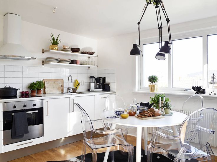 czarna lampa z trzema wysięgnikami w kuchni nad stołem,transparentne przeźroczyste krzesła w kuchni,przexroczyste bezbarwne krzesła w kuchni,okragły biały stół do kuchni w stylu nowoczesnym,nowoczesny okragły stół biały