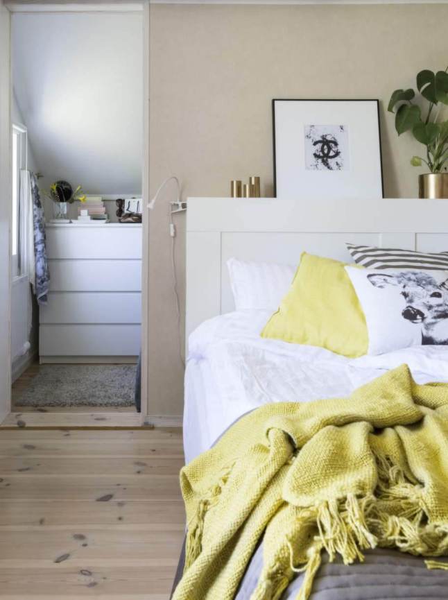 białe łóżko w sypialni,żółty koc,żółty pled z fredzlami,sypialnia w stylu skandynawskim,żółta poduszka,poduszka z graficznym wzorem i ilustracją