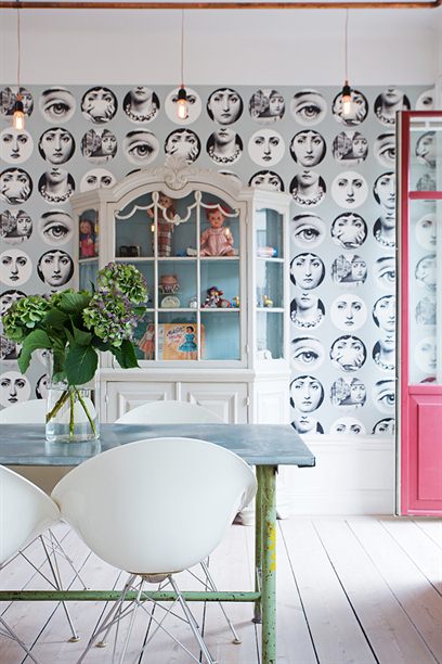 różowe drzwi w jadalni,nowoczesne krzesła na metalowym krzyżaku,białe krzesła z poliuretanu,aranżacja jadalni w eklektycznym stylu,ekskluzywna tapeta na scianie,tapeta z rysunkami Piero Fornasetti,twarze na tapetach